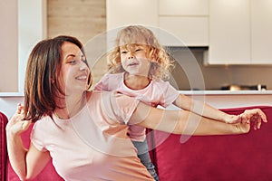 Girl wanna have fun. Young mother with her little daughter in casual clothes together indoors at home