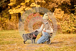 A girl in warm clothes playing with a dog in the park