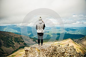 a girl in warm clothes stands with her back on the top with beautiful mountains and lakes