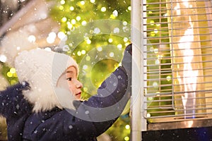 Girl in a warm hat looks at the flame of a gas burner warming at a Christmas market in the city, warms your hands. lights of