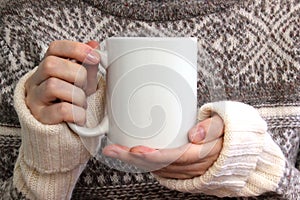 Girl in a warm sweater is holding white mug in hands. photo