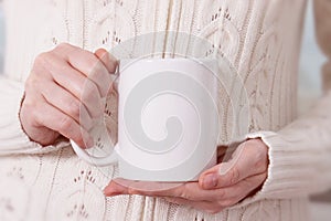 Girl in warm sweater is holding white mug in hands. photo