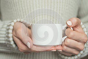 Girl in warm sweater is holding white mug in hands.. Mockup for winter gifts design