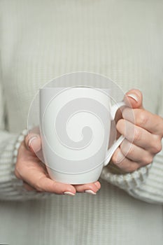 Girl in warm sweater is holding white mug in hands.. Mockup for winter gifts design.