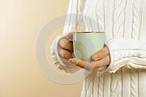 Girl in warm sweater is holding white mug in hands.. Mockup for winter gifts design. Space text.