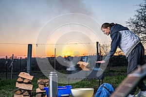 Girl warms up near open fire. Woman holds hands above flame to toast herself. Burning woods logs and charcoal are in