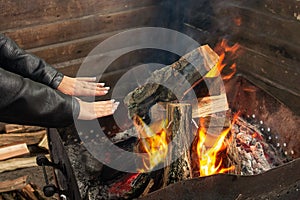 Girl warms up near open fire. Woman holds hands above flame to toast herself. Burning woods logs and charcoal are in barbecue