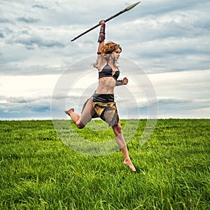 Girl warrior in the field.Jump with a spear.