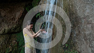 Girl washes her face under the waterfall in the woods. Young woman in swimsuit in mountain river
