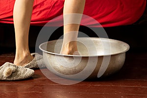 a girl washes her feet in an aluminum basin with water on a wooden floor at home, foot care, wash feet at home, hygiene