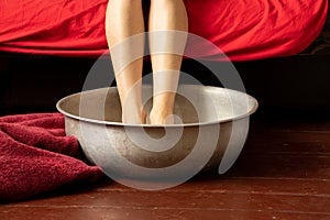 a girl washes her feet in an aluminum basin with water on a wooden floor at home, foot care, wash feet at home, hygiene