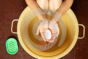 a girl washes her feet in a basin of water on a wooden floor at home, care for her feet, wash her feet at home, soap in