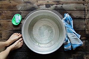 girl washes her feet in a basin of water on the wooden floor at home, foot care, wash feet at home, hygiene, swim