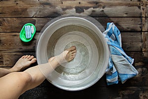 girl washes her feet in a basin of water on the wooden floor at home, foot care, wash feet at home, hygiene, swim