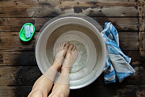 girl washes her feet in a basin of water on the wooden floor at home, foot care, wash feet at home, hygiene, swim
