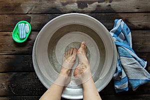 girl washes her feet in a basin of water on the wooden floor at home, foot care, wash feet at home, hygiene, swim