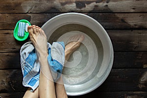 girl washes her feet in a basin of water on the wooden floor at home, foot care, wash feet at home, hygiene, swim