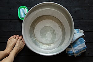 girl washes her feet in a basin of water on the wooden floor at home, foot care, wash feet at home, hygiene, swim