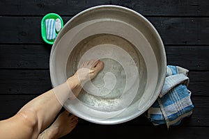 girl washes her feet in a basin of water on the wooden floor at home, foot care, wash feet at home, hygiene, swim