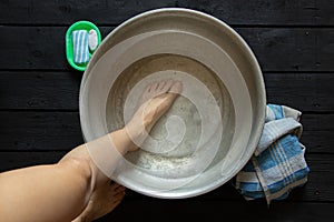 girl washes her feet in a basin of water on the wooden floor at home, foot care, wash feet at home, hygiene, swim