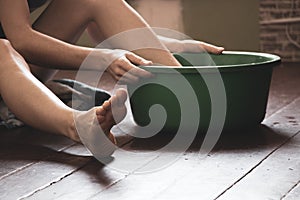 A girl washes her feet in a green basin with water on a wooden floor at home, foot care, wash her feet at home, hygiene, swim