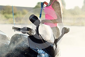 Girl washes a motorcycle in self service car wash with high pressure water jet.