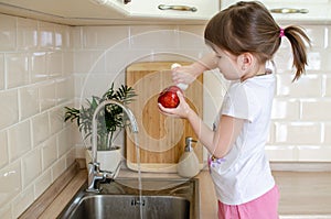 Girl washes a red apple in the kitchen near the sink. The concept of children`s health and independence