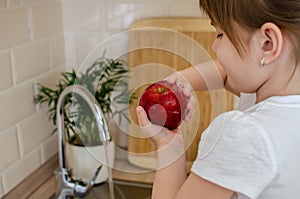 Girl washes a red apple in the kitchen near the sink. The concept of children`s health and independence