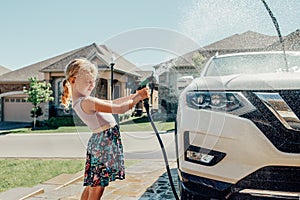 Girl washing car on driveway in front house on sunny summer day