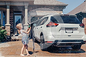 girl washing car on driveway in front house on sunny summer day