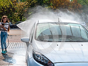 Girl washing car with water and hose at a do it yourself car wash