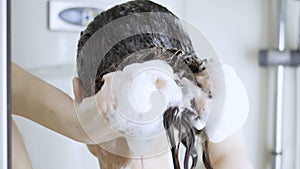 A girl is washing her hair. White foam from the shampoo on long hair brunettes