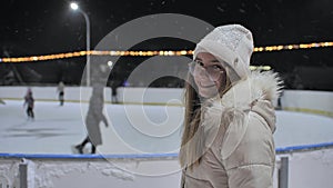 A girl watches people on a skating rink in the city.