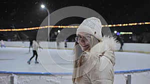 A girl watches people on a skating rink in the city.