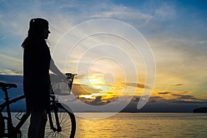 girl watching the horizon with a bike on a beautiful sunset on the sea