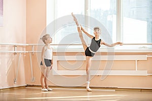 Girl watching older ballet student practicing at barre