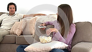 Girl watching tv with popcorn while her boyfriend listens to music