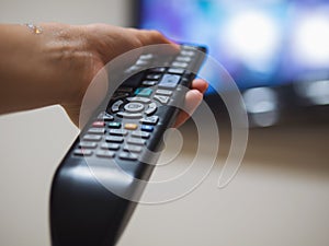 Girl watching tv on the sofa. Young woman turns on the television with the remote control. Only hand