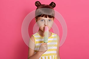 Girl with water ice cream looking directly at camera, posing isolated over pink background, wearing striped white and yellow