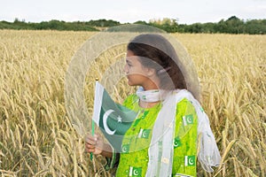 Girl waving flag of Pakistan outdoors over blue cloudy sky and golden wheat.