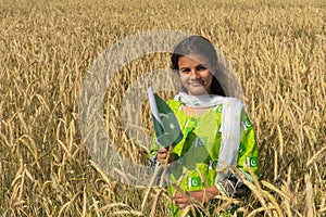 Girl waving flag of Pakistan outdoors over blue cloudy sky and golden wheat.