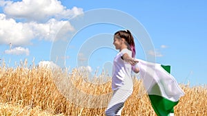 Girl waving flag of Pakistan outdoors over blue cloudy sky and golden wheat. Day of Pakistan