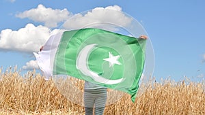 Girl waving flag of Pakistan outdoors over blue cloudy sky and golden wheat. Day of Pakistan