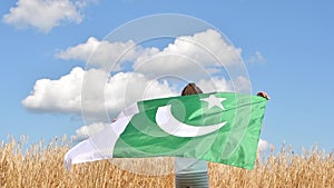 Girl waving flag of Pakistan outdoors over blue cloudy sky and golden wheat. Day of Pakistan