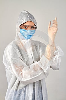 Girl wearing antiviral protective uniform putting on rubber gloves.