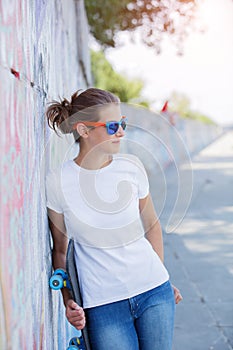 Girl wearing blank white t-shirt, jeans posing against rough street wall