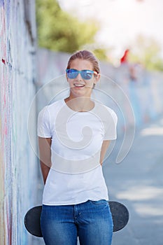 Girl wearing blank white t-shirt, jeans posing against rough street wall