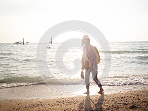 Girl wearing Blue jeans and red plaid shirt and backpacking yellow doing walking on the sea