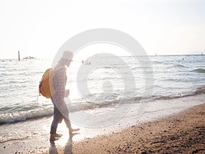 Girl wearing Blue jeans and red plaid shirt and backpacking yellow doing walking on the sea