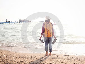 Girl wearing Blue jeans and red plaid shirt and backpacking yellow doing walking on the sea